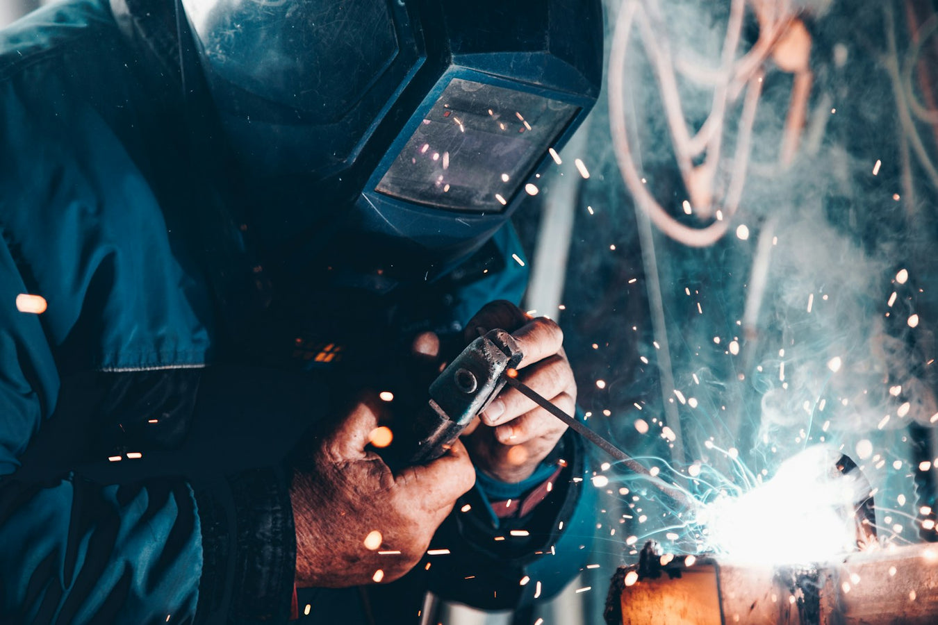 A welder wearing a welding helmet works on metal with sparks flying.
