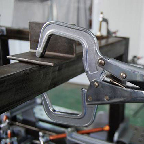 Strong Hand Tools PR115 locking C-clamp holding an angled steel piece against a steel beam on a workbench.